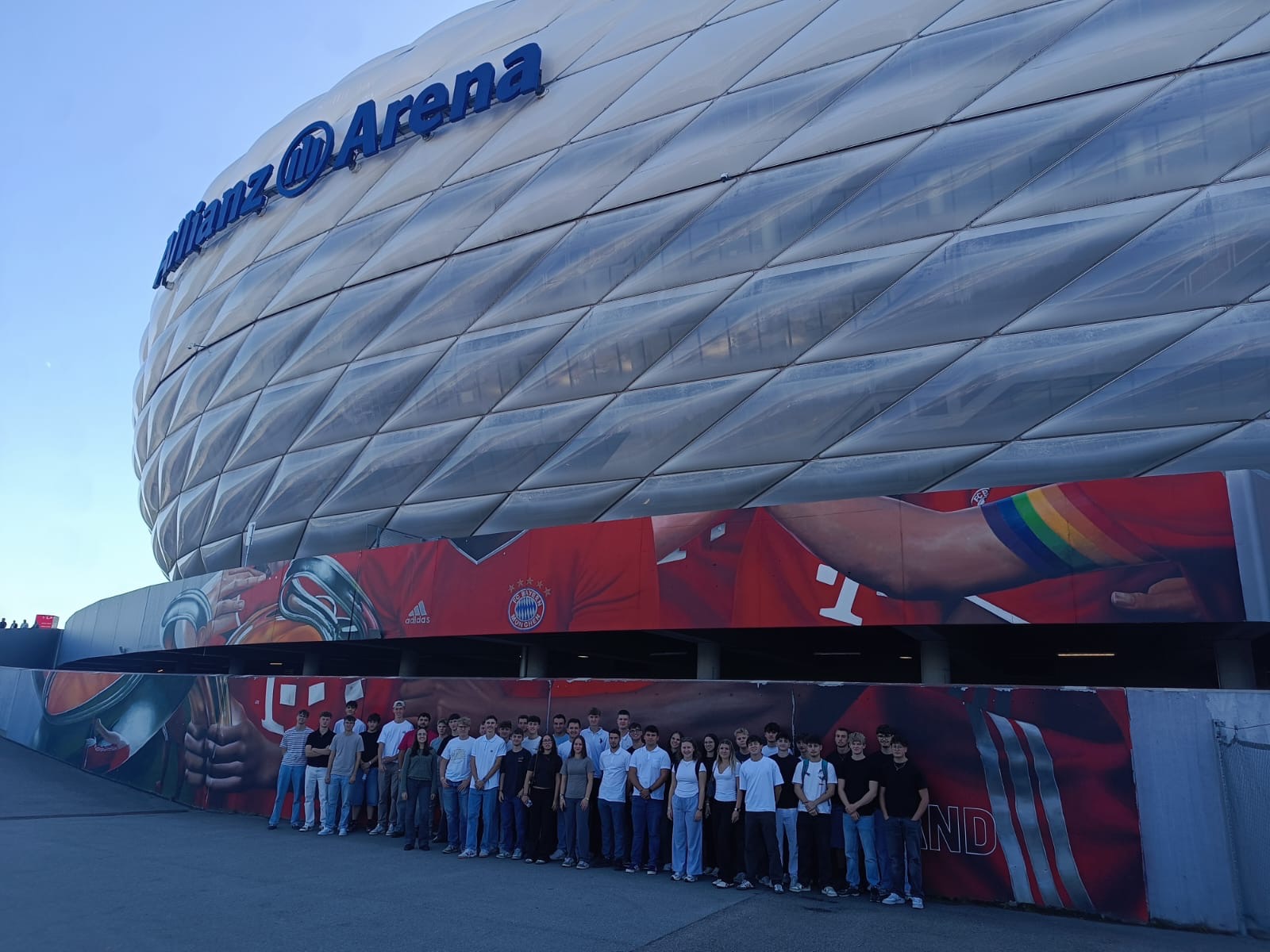 Allianz Arena in München mit einer Gruppe junger Leute vor einer Wandmalerei.