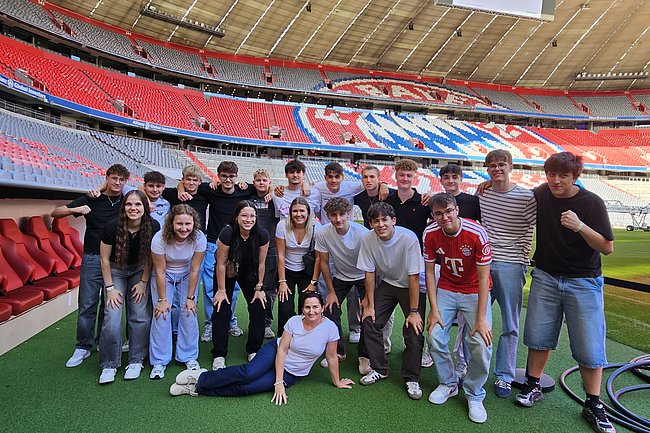 Jugendliche und eine Frau posieren im Stadion des FC Bayern München.